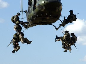 Canadian soldiers rappel from a hovering helicopter.