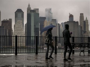 Passersby walk along the Promenade in the Brooklyn Heights neighborhood as rain and clouds loom over lower Manhattan on the fifth anniversary of Superstorm Sandy Sunday, Oct. 29, 2017, in New York.