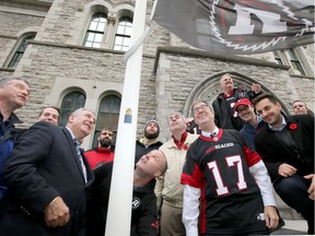 Ottawa Redblacks coach Rick Campbell hoists the team flag at City Hall as some of his players, mayor Jim Watson and city council honour of the upcoming playoffs and Grey Cup match coming here to the city.