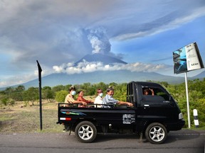 Balinese people ride on an open car past Mount Agung erupting seen from Kubu sub-district in Karangasem Regency, on Indonesia's resort island of Bali on November 27, 2017.