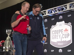 Toronto Argonauts head coach Marc Trestman puts his arm around Calgary Stampeders head coach Dave Dickenson as they talk leaving the stage following the head coaches news conference Wednesday. THE CANADIAN PRESS/Adrian Wyld