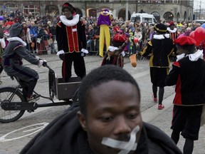 A demonstrator turns his back to the parade of Sinterklaas, the Dutch version of Santa Claus, and his blackfaced sidekick  'Zwarte Piet', or Black Pete, rear, in Amsterdam in 2013.