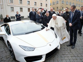Pope Francis writes on the bonnet of a Lamborghini donated to him by the luxury sports car maker, at the Vatican, Wednesday, Nov. 15, 2017. The car will be auctioned off by Sotheby's, with the proceeds going to charities including one aimed at helping rebuild Christian communities in Iraq that were devastated by the Islamic State group. (L'Osservatore Romano/Pool Photo via AP)