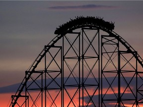 People ride a roller coaster at dusk.