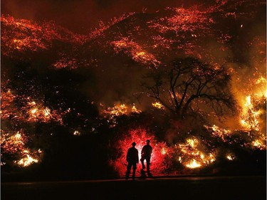 Firefighters monitor a section of the Thomas Fire along the 101 freeway on December 7, 2017 north of Ventura, California. The firefighters occasionally used a flare device to burn-off brush close to the roadside. Strong Santa Ana winds are rapidly pushing multiple wildfires across the region, expanding across tens of thousands of acres and destroying hundreds of homes and structures.