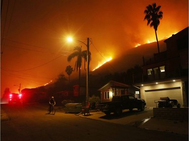 LA CONCHITA, CA - DECEMBER 07:  A person bicycles as a section of the Thomas Fire burns on a bluff on December 7, 2017 in La Conchita, California. Many evacuation holdouts were forced to flee the small seaside town as the flames approached. Strong Santa Ana winds are rapidly pushing multiple wildfires across the region, expanding across tens of thousands of acres and destroying hundreds of homes and structures.