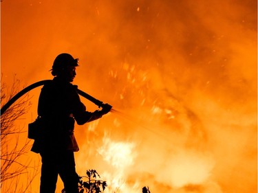 TOPSHOT - A firefighter battles a wildfire as it burns along a hillside near homes in Santa Paula, California, on December 5, 2017.  Fast-moving, wind-fueled brush fire exploded to about 10,000 acres in Ventura County Monday night, forcing hundreds of people to flee their homes, officials said.