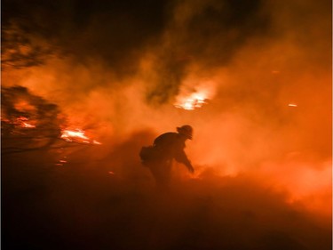 A firefighter battles a wildfire as it burns along a hillside near homes in Santa Paula, California, on December 5, 2017. Fast-moving, wind-fueled brush fire exploded to about 10,000 acres in Ventura County Monday night, forcing hundreds of people to flee their homes, officials said.