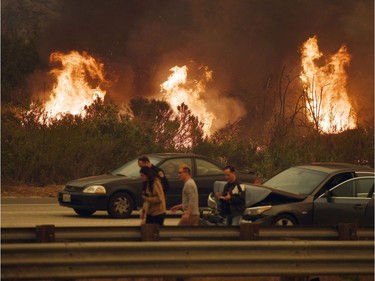 TOPSHOT - A woman involved in a traffic accident waits to get towed beside a wall of flames on the 101 highway during the Thomas wildfire near Ventura, California on December 6, 2017.  California motorists commuted past a blazing inferno Wednesday as wind-whipped wildfires raged across the Los Angeles region, with flames  triggering the closure of a major freeway and mandatory evacuations in an area dotted with mansions.