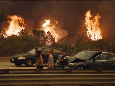 A woman involved in a traffic accident waits to get towed beside a wall of flames on the 101 highway during the Thomas wildfire near Ventura, California on December 6, 2017.  California motorists commuted past a blazing inferno Wednesday as wind-whipped wildfires raged across the Los Angeles region, with flames  triggering the closure of a major freeway and mandatory evacuations in an area dotted with mansions.
