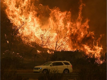 Vehicles pass beside a wall of flames on the 101 highway as it reaches the coast during the Thomas wildfire near Ventura, California on December 6, 2017. California motorists commuted past a blazing inferno Wednesday as wind-whipped wildfires raged across the Los Angeles region, with flames  triggering the closure of a major freeway and mandatory evacuations in an area dotted with mansions.