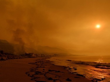 TOPSHOT - Heavy smoke covers the seaside enclave of Mondos Beach beside the 101 highway as flames reach the coast during the Thomas wildfire near Ventura, California on December 6, 2017. California motorists commuted past a blazing inferno Wednesday as wind-whipped wildfires raged across the Los Angeles region, with flames  triggering the closure of a major freeway and mandatory evacuations in an area dotted with mansions.