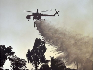 A helicopter drops water on the Skirball Fire in west Los Angeles, California, December 6, 2017. California motorists commuted past a blazing inferno Wednesday as wind-whipped wildfires raged across the Los Angeles region, with flames  triggering the closure of a major freeway and mandatory evacuations in an area dotted with mansions.