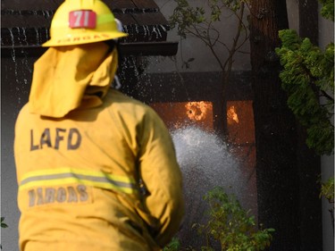 A firefighter controls flames burning in a home at the Skirball Fire in the upscale Bel Aire section of west Los Angeles, California, December 6, 2017. California motorists commuted past a blazing inferno Wednesday as wind-whipped wildfires raged across the Los Angeles region, with flames  triggering the closure of a major freeway and mandatory evacuations in an area dotted with mansions.