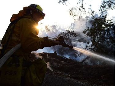 TOPSHOT - A firefighter controls flames burning in a home at the Skirball Fire in the upscale Bel- Air section of west Los Angeles, California, December 6, 2017. California motorists commuted past a blazing inferno Wednesday as wind-whipped wildfires raged across the Los Angeles region, with flames  triggering the closure of a major freeway and mandatory evacuations in an area dotted with mansions.