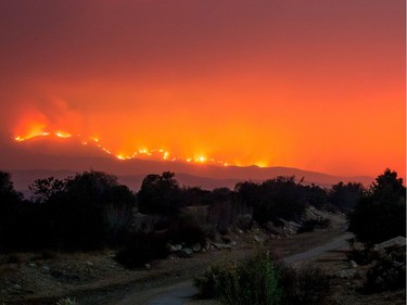 The Thomas Fire burns behind trails on Old Baldwin Road in Ojai, California on December 6, 2017. Local emergency officials warned of powerful winds on December 7 that will feed wildfires raging in Los Angeles, threatening multi-million dollar mansions with blazes that have already forced more than 200,000 people to flee.