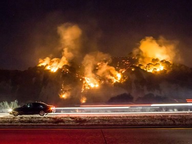 A car drives past as the Thomas Fire burns a hillside south of Casitas Springs, California, December 6, 2017. Local emergency officials warned of powerful winds on December 7 that will feed wildfires raging in Los Angeles, threatening multi-million dollar mansions with blazes that have already forced more than 200,000 people to flee.