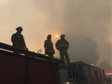 Los Angeles firefighters stand on a fire engine during sunrise as they battle flames on Casiano Road after the Skirball fire swept through the Bel Air district of Los Angeles, Wednesday, Dec. 6, 2017.
