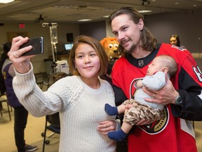 Kayla Kooneeliusie takes a selfie while Erik Karlsson holds her 2 month old son Sheldon in his arms as the Ottawa Senators make their annual holiday visit to CHEO to bring a little cheer into the lives of patients, their parents and a few of the staff at the childrens hospital.