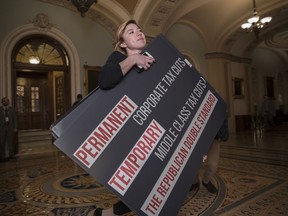 An aide for Sen. Ron Wyden, D-Ore., carries a poster that he used on the Senate floor to criticize the Republican tax bill, on Capitol Hill in Washington, Friday, Dec. 1, 2017.