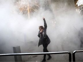 TOPSHOT - An Iranian woman raises her fist amid the smoke of tear gas at the University of Tehran during a protest driven by anger over economic problems, in the capital Tehran on December 30, 2017. Students protested in a third day of demonstrations sparked by anger over Iran's economic problems, videos on social media showed, but were outnumbered by counter-demonstrators.