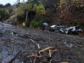 A firefighter (in yellow) instructs journalists to retreat to safer ground after a rain-driven mudslide destroyed two cars and damaged property in a neighborhood under mandatory evacuation in Burbank, California, January 9, 2018. Mudslides unleashed by a ferocious storm demolished homes in southern California, authorities said Tuesday. Five people were reported killed.