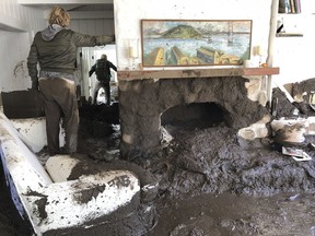 In this photo provided by Santa Barbara County Fire Department, Teresa Drenick stands in her sister's home damaged after heavy rains off Glen Oaks Lane, while Sean Bornwell retrieves some of her sister's personal belongings on Wednesday, Jan. 10, 2018, in Montecito, Calif.