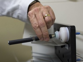 FILE - In this Thursday, Nov. 10, 2016 file photo, a doctor holds an e-cigarette in a smoking lab at the Centers for Disease Control and Prevention in Atlanta. An exhaustive government report issued Tuesday, Jan. 23, 2018 wrestles with the potential benefits and harms of the vapor-emitting devices, which remain unclear more than a decade after their introduction in the U.S.