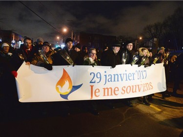 Prime Minister Justin Trudeau, middle left to right, Quebec City mayor Regis Labeaume and Quebec Premier Philippe Couillard march with a banner during a vigil to commemorate the one-year anniversary of the Quebec City mosque shooting in Quebec City, Monday, Jan. 29, 2018.