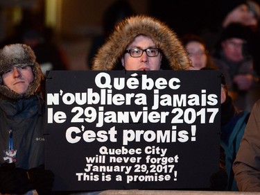 A man holds a sign at a vigil to commemorate the one-year anniversary of the Quebec City mosque shooting, in Quebec City, Monday, Jan.29, 2018.