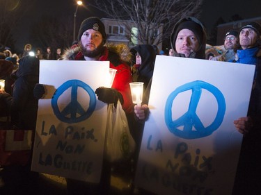 People hold peace signs at a vigil to commemorate the one-year anniversary of the Quebec City mosque shooting, in Quebec City, Monday, Jan. 29, 2018.