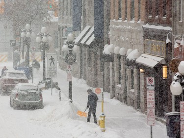 A person clears the snow from the sidewalk on York St as the region experiences continuing snowfall on Monday.