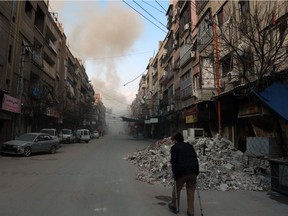 A Syrian man on crutches walks down a street as smoke billows in the rebel-held town of Douma, in the besieged Eastern Ghouta region on the outskirts of the capital Damascus, following air strikes by regime forces on the area on Feb. 23.