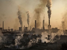 Smoke billows from a large steel plant as a Chinese labourer works at an unauthorized steel factory, foreground, on November 4, 2016 in Inner Mongolia, China. To meet China's targets to slash emissions of carbon dioxide, authorities are pushing to shut down privately owned steel, coal, and other high-polluting factories scattered across rural areas. In many cases, factory owners say they pay informal 'fines' to local inspectors and then re-open.