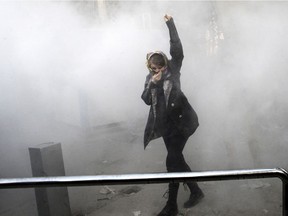 In this Dec. 30, 2017 photo made by an individual not employed by the Associated Press and obtained by the AP outside Iran, a university student attends a protest inside Tehran University while a smoke grenade is thrown by Iranian police.