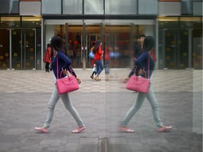 A woman is reflected in a window as she walks past a mall.