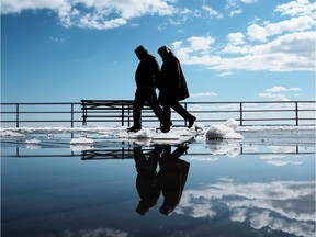 A couple walks by puddles from snow melt.