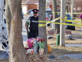 A police officer carries flowers outside a residence in Ajax, Ont., on Thursday, March 15, 2018, from a sympathizer for the victims of a triple slaying. Autopsies on three members of a family killed at their home last week show two were stabbed and one was strangled.