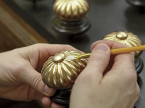 In this photo provided by Ethan Allen, a craftsman uses a small artists brush to press the gold leafing material into the detailed carved elements of the finial on an Ethan Allen Georgetown Bed in their North American workshops. (Ethan Allen via AP)