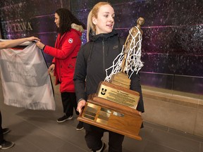 Nicole Gilmore hoists 'The Bronze Baby' after the Carleton Ravens women's basketball team flew into the Ottawa Macdonald-Cartier Airport Monday. (Wayne Cuddington/Postmedia)