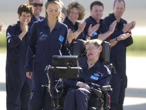 FILE - Astrophysicist Stephen Hawking is assisted off the tarmac at the Kennedy Space Center by his caregiver, Monica Guy, as he is applauded by members of the flight crew after completing a zero-gravity flight, Thursday, April 26, 2007, in Cape Canaveral, Fla. Hawking, whose brilliant mind ranged across time and space though his body was paralyzed by disease, has died, a family spokesman said early Wednesday, March 14, 2018.