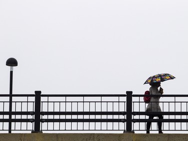 Sunday afternoon Ottawa was just starting to see the effects of the winter storm that has hit other parts of Ontario hard. A pedestrian makes her way along Mackenzie King Bridge as the rain started Sunday April 15, 2018.   Ashley Fraser/Postmedia