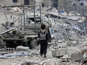 TOPSHOT - A Syrian boy walks past debris, rubble, and a damaged vehicle in the town of Hazzeh in Eastern Ghouta, on the outskirts of the Syrian capital Damascus, on March 28, 2018.