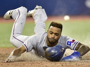 Texas Rangers centre fielder Delino DeShields (3) slides in to score as the throw from the outfield goes astray during ninth inning American League baseball action against the Blue Jays in Toronto, Saturday, April 28, 2018.