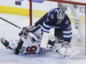 Winnipeg Jets goaltender Connor Hellebuyck (37) gets taken down by Minnesota Wild's Jason Zucker (16) during third period game five NHL playoff action in Winnipeg on Friday, April 20, 2018.