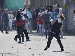 A masked Kashmiri youth throws stones on government forces during a protest in Srinagar, India, Thursday, April 12, 2018. Indian forces used tear gas and pellet guns to disperse stone-throwing youth who were protesting against killing of three civilians Wednesday.