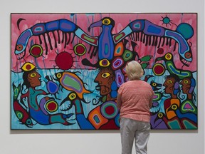 A woman surveys the painting "Copper Thunderbird" by Norval Moreisseau on display.