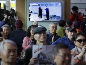 People watch a TV screen showing the live broadcast of South Korean President Moon Jae-in, top right, meets with North Korean leader Kim Jong Un at the border village of Panmunjom during a news program at the Seoul Railway Station in Seoul, South Korea, Friday, April 27, 2018.