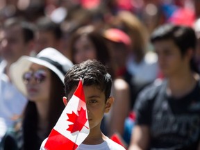 A young boy holds a Canadian flag while watching a special Canada Day citizenship ceremony in B.C., on July 1, 2017.