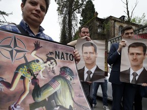 People hold pictures of Syrian President Bashar al-Assad and an anti NATO poster during a protest outside the Syrian embassy in Belgrade, Serbia, Sunday, April 15, 2018. A few dozen people took part in an anti-war rally opposing the military strikes by western countries in Syria.